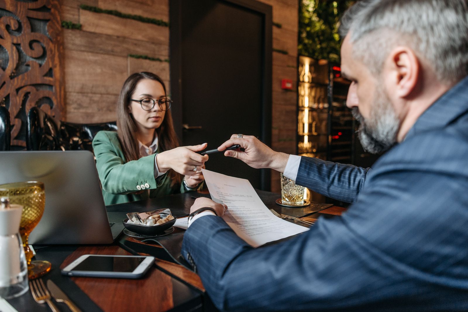 Woman passing a pen across a table to a man reading a contract